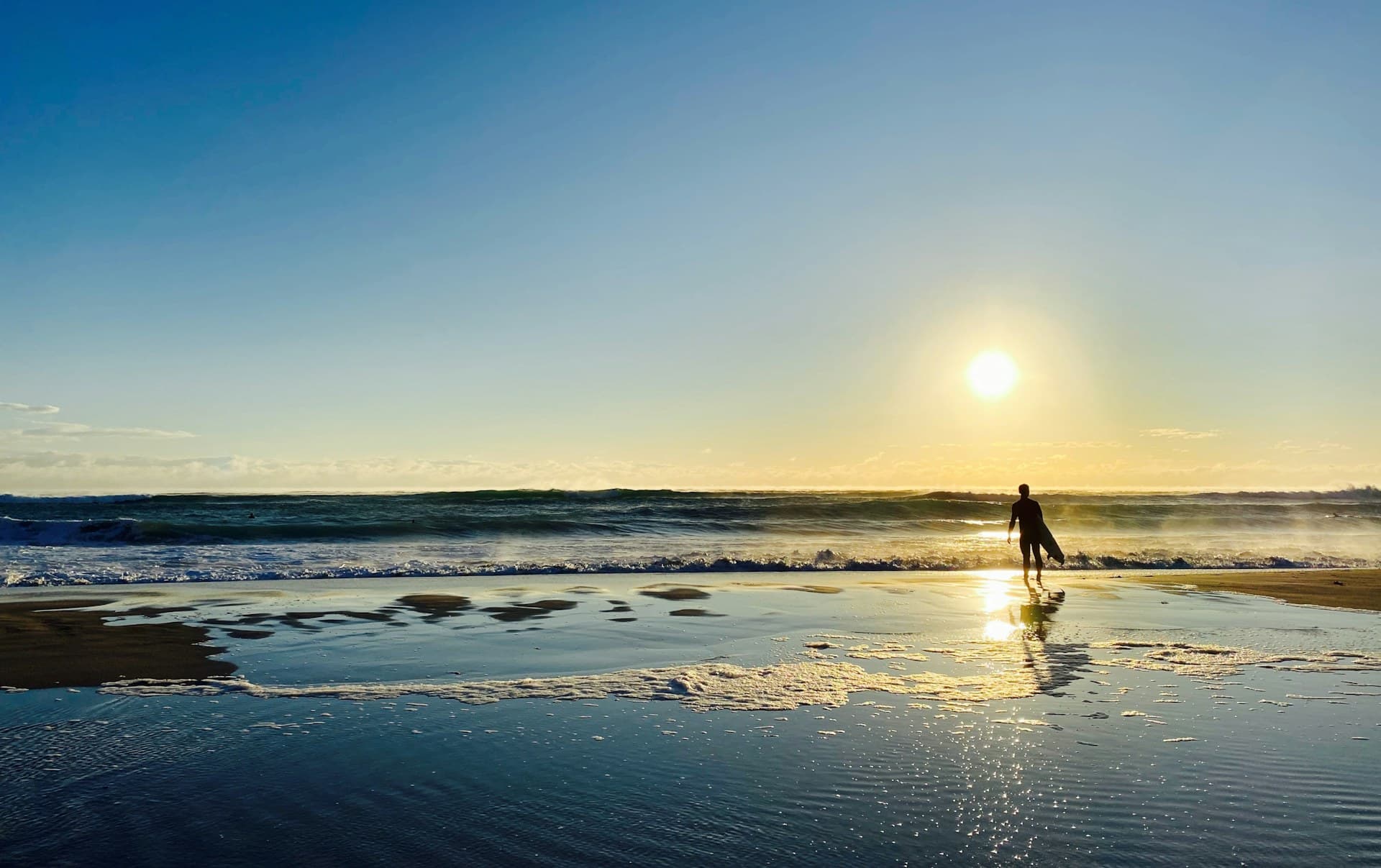 A surfer walks the shoreline at sunrise in Palm Beach