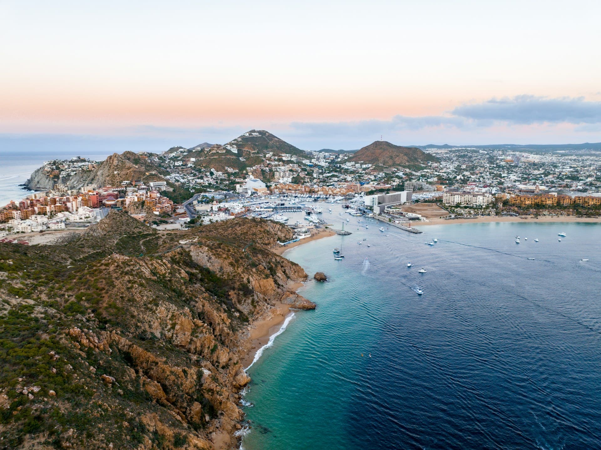 Aerial view of Cabo San Lucas, its marina, and the bay under a pastel sky