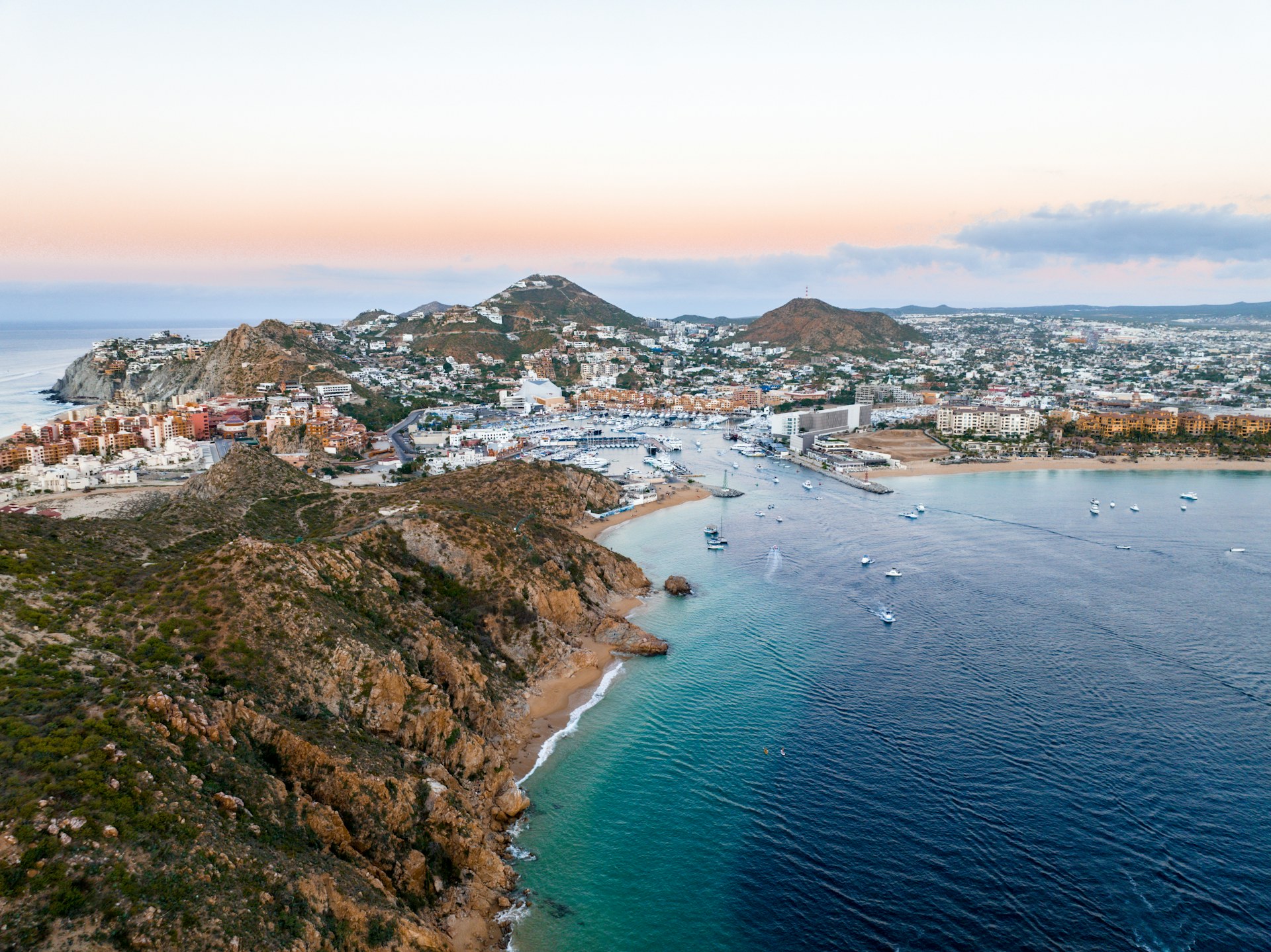 Aerial view of Cabo San Lucas, its marina, and the bay under a pastel sky